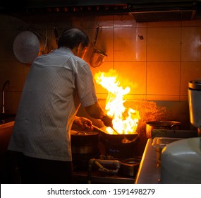 Chef cooking with fire in a hawker centre kitchen in Singapore