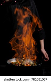 Chef Cooking With Fire Pan. Black Background For Copy Text. Vertical Photo For Banner Design.