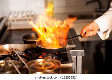 Chef Cooking With Flame In A Frying Pan On A Kitchen Stove.