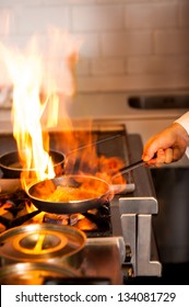 Chef Cooking With Flame In A Frying Pan On A Kitchen Stove.