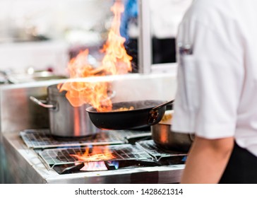 Chef cooking with flame in a frying pan on a kitchen stove - Shutterstock ID 1428621314