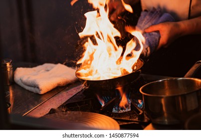 Chef cooking with flame in a frying pan on a kitchen stove