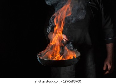 Chef cooking food in pan with fire flame on black background. Restaurant and hotel service concept. Free advertising space - Shutterstock ID 1970698700