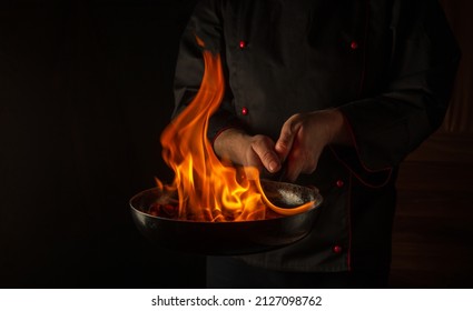The chef cooking food in pan with fire flame on black background. Restaurant and hotel service concept. Asian cuisine. - Powered by Shutterstock