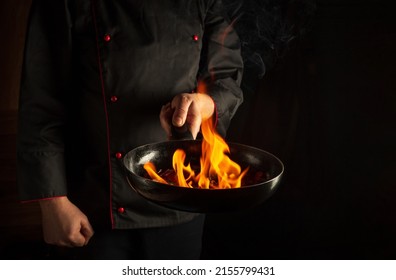 The chef cooking food in pan with fire flame on black background. Restaurant and hotel service concept. European cuisine - Powered by Shutterstock