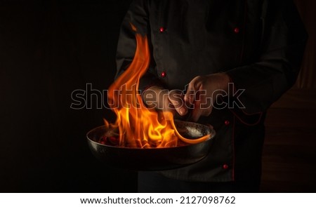 The chef cooking food in pan with fire flame on black background. Restaurant and hotel service concept. Asian cuisine.