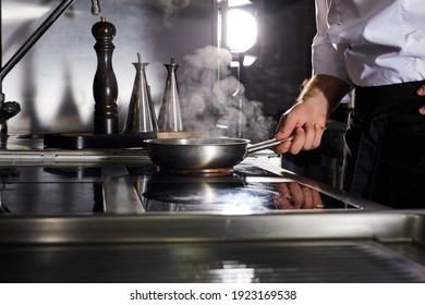 Chef cooking in frying pan on kitchen stove, cropped unrecognizable cook preparing food. steam comes from pan