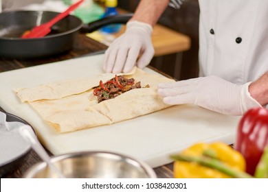 Chef cooking mexican burrito. Chef hands wrapping burrito filling in tortilla. The process of preparing mexican burrito at kitchen. - Powered by Shutterstock