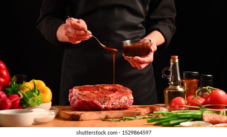 Chef Is Cooking Pork Steak. Pouring Sauce, Marinade On A Background With Vegetables. Recipe Book, Cooking, Restaurant Business