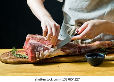 The chef cooking raw goat leg on a wooden chopping Board. Rosemary, thyme, black pepper. Black background, side view, space for text - Powered by Shutterstock