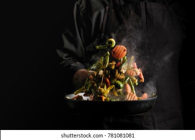 Chef cooking vegetables on a pan. Black background for copy text. - Shutterstock ID 781081081