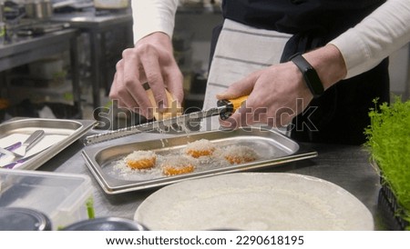 Chef cooks delicious meal on kitchen. Male cook grates cheese on baked sweet potato using small cheese grater. Process of cooking gourmet dish. Restaurant with professional cuisine. Public catering.