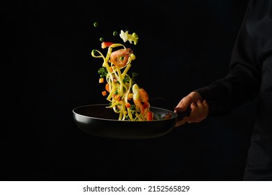 The chef cooks seafood with italian pasta in a frying pan on a black background. Frozen in-flight food. There is free space to insert. Sea food. Healthy vegetarian food recipes.