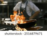 A chef creates a burst of flames while tossing food in a pan, displaying a dramatic cooking technique in the hotel