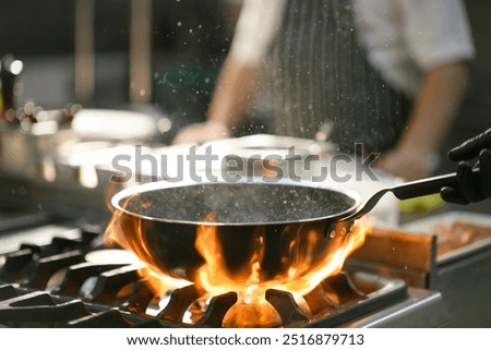 A chef creates a burst of flames while tossing food in a pan, displaying a dramatic cooking technique in the hotel's kitchen