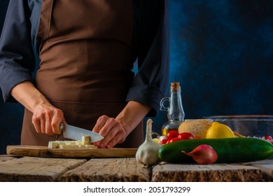 The Chef Cuts The Cheese On A Cutting Board. Ingredients For Making A Classic Greek Salad. Close-up. Wooden Texture. Vitamin Dietary Dish. Low In Calories. Restaurant, Hotel, Home Cooking.