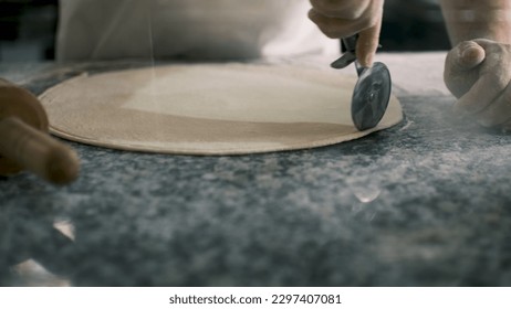 The chef cuts the edges of the round-shaped dough with a special roller.View behind glass - Powered by Shutterstock