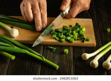 A chef cuts green garlic on a cutting board with a knife to prepare a vegetable dish for lunch. - Powered by Shutterstock