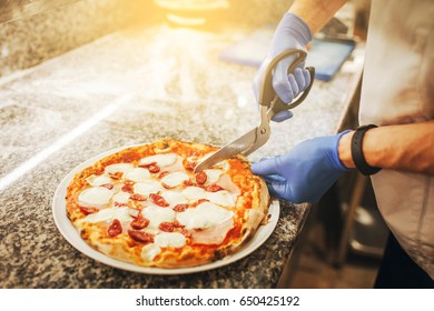 Chef Cuts Pizza With Kitchen Scissors.