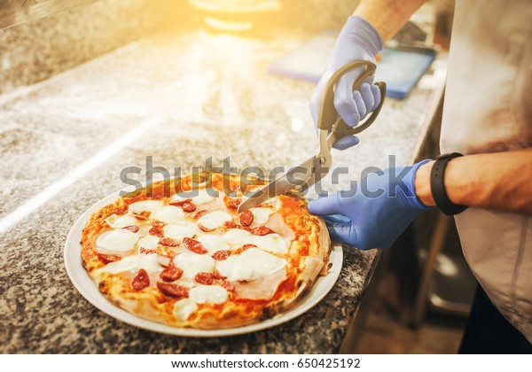 Chef cuts pizza with\
kitchen scissors.