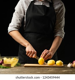 The chef cuts the potatoes for mashed potatoes, stews, fried and with vegetables. For dishes with potatoes. On a black background, the concept of the menu, cooking, healthy eating