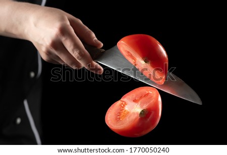 Chef cuts a tomato a knife on the fly on a black background. The concept of cooking and profession. 