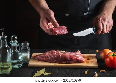 The chef cutting beef meat with knife on kitchen, cooking food. Vegetables and spices on kitchen table to prepare delicious lunch