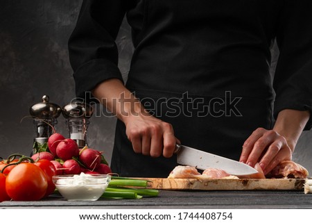 Chef cutting chicken meat, ingredients for cooking on a background of vegetables. Culinary recipes, cookbooks