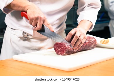 Chef Cutting A Large Raw Boneless Beef Steak Meat On A White Cutting Board.