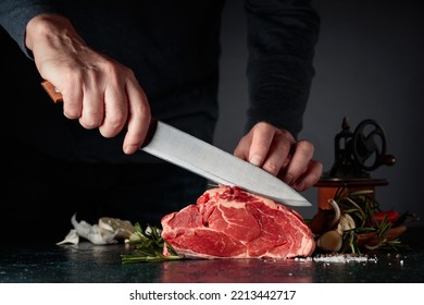 Chef cutting raw beef meat. On a table meat with rosemary, garlic, salt, and pepper. - Powered by Shutterstock