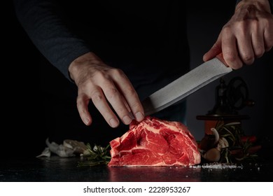 Chef cutting raw beef meat. On a table meat with rosemary, garlic, salt, and pepper. - Powered by Shutterstock