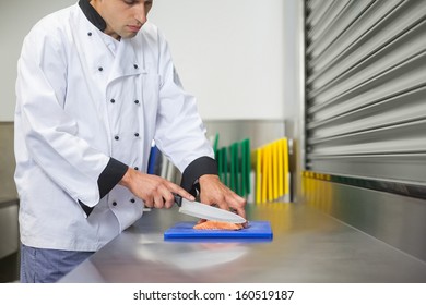 Chef cutting raw salmon with knife on blue cutting board in professional kitchen