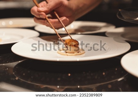 Chef decorates the dish. Professional chef adding scallop  to white plate.