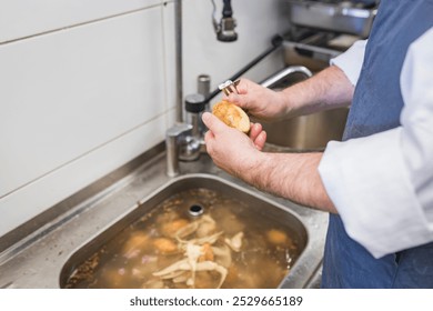 A chef efficiently peels potatoes over a sink in a professional kitchen, showcasing culinary preparation techniques and attention to detail, essential for cooking delicious meals. - Powered by Shutterstock