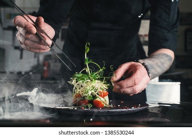 Chef finishing healthy salad on a black plate with tweezers. almost ready to serve it on a table - Powered by Shutterstock