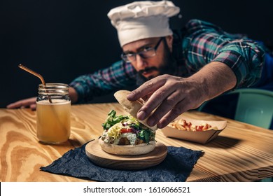 Chef Finishing Up His Vegan Burger With Lettuce Tomato And Sauce, Fries With Ketchup And Healthy Drink On A Wooden Table, Vegetarian Food And Foodie Lifestyle Concept, Selective Focus