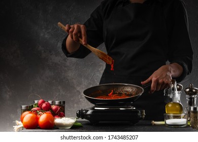 The Chef Fries Tomatoes Making Sauce For Pizza Or Italian Pasta. Against The Background Of Ingredients, Tasty And Healthy Nutrition