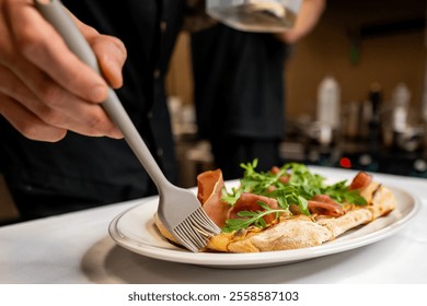 A chef garnishes a freshly baked flatbread with prosciutto and arugula using a brush. The elegant presentation showcases culinary skill in a modern kitchen setting. - Powered by Shutterstock