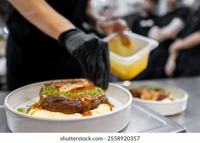 A chef garnishes a plate of steak served on creamy mashed potatoes, drizzled with rich sauce. The vibrant kitchen setting adds to the culinary experience, showcasing a passion for gourmet cooking. - Powered by Shutterstock