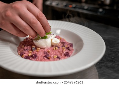 A chef garnishes a vibrant pink risotto with a poached egg, fresh herbs, and pine nuts. The dish is presented elegantly on a white plate, showcasing culinary creativity. - Powered by Shutterstock