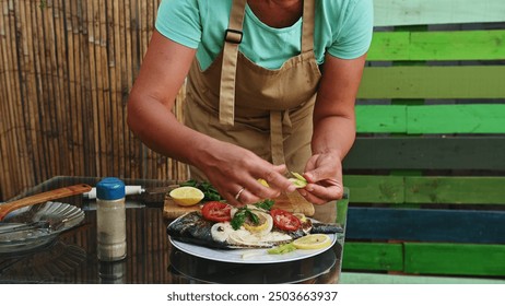 A chef garnishing grilled fish with fresh vegetables and lemon in an outdoor setting. Culinary art, summer barbecue, and gourmet cooking come alive in this vibrant scene. - Powered by Shutterstock