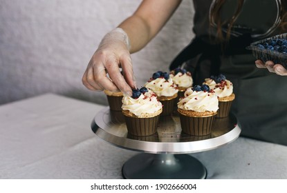 the chef girl decorates fresh cupcakes covered with vanilla cream with berries.Sweet homemade cupcakes with cream on a tray. Food for breakfast. Freshly baked cupcakes for dessert. - Powered by Shutterstock