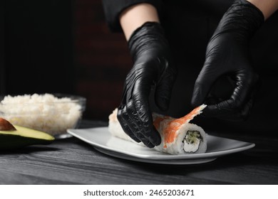 Chef in gloves making sushi rolls with shrimps at black wooden table, closeup - Powered by Shutterstock