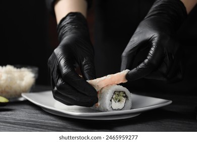 Chef in gloves making sushi rolls with shrimps at black wooden table, closeup - Powered by Shutterstock