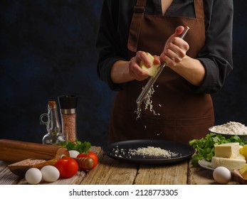 The chef grates cheese. Ingredients for making salad, pizza, risotto. Recipes, cooking, restaurant, hotel. cafe, home cooking, advertising. Dark background, wooden texture. - Powered by Shutterstock