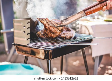 Chef grill t-bone steaks at barbecue dinner outdoor - Man cooking meat for a family bbq meal outside in backyard garden - Summe lifestyle, food and sunday time concept - Focus on tongs