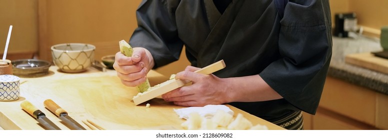 Chef grinding fresh wasabi on a wooden grater.