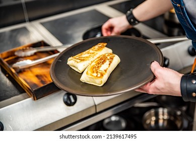 chef hand cooking Thin pancakes crepe rolls with ground meat in pan at a restaurant kitchen