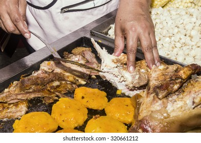 Chef hand showing typical Ecuadorian food preparation, pieces of pork and potato cakes llapingachos being fried in large frying pan.