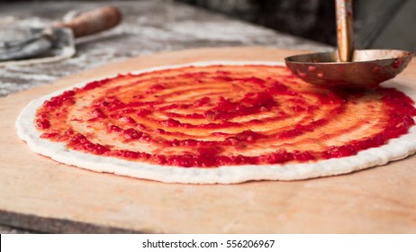 Chef hand is spreading pasteurized tomato paste onto a Pizza base  - Powered by Shutterstock